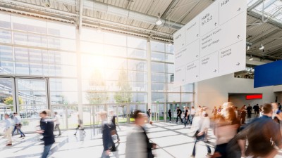 Modern venvention hall interior with glass walls overlooking a plaza, bustling with poeple moving in dynamics directions.